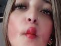 AlessadraJoness has pouty red lips, a nose ring, and long eyelashes. She's sucking her bottom lip with flushed cheeks. Her blonde hair is slightly visible.