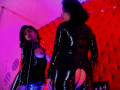 RoxanneHan with dark hair, wearing a shiny black latex outfit, showing a butt cutout, stands in front of a mirror. Reflection shows her looking down at her tits.