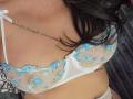 Seins de Shanna, visibles à travers un soutien-gorge floral blanc et bleu transparent, révélant un tatouage sur sa poitrine, avec des cheveux noirs ondulés partiellement visibles..