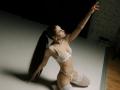 MilagrosEdmisten with long black ponytail, white lace bra, and panties, white thigh-highs, kneeling, arm raised, red lipstick, slim, small tits, pale skin, in dimly lit room.