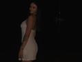 Olieri has a curvy body, wearing a tight white dress, showing her ass and small tits, with long black hair, a tattoo on her right arm, and a watch.