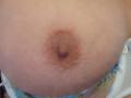 Seins de Shanna, situés au centre du cadre, montrant une aréole brun clair et un mamelon légèrement relevé sur une peau pâle. Le bord inférieur d'un vêtement en dentelle blanche et bleue est visible..