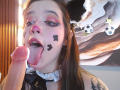 AryButty with cat ears, pink eyeshadow, and black face paint, tongue out, licking a large, erect, circumcised penis with a shiny tip. Tattoos visible on her right arm.