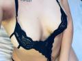LonxEva's tits in a black lace bra, showing her cleavage and a tattoo above her chest. Her right arm crosses her lower belly. Light-skinned, soft skin, slight tan.