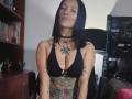 AmelieBlake with black bob, nose ring, choker, black bra, showing tattoos on arms and chest, and colorful tattoo on lower belly, smiling slightly. Boobs, arms tattoos, belly tattoo.