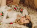 KylaHemeke lying on a bed, wearing a white lace dress, pearl necklace, and red roses, with her blonde hair spread out, her hand near her face, and her tits visible.