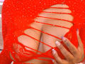 Genexis wears a red, cut-out, polka-dot top, revealing large, lacy red bra-covered tits, with manicured nails and tattooed hand pulling top.