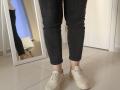 Elliance's legs in black jeans, white quilted sneakers, standing on white tile floor, with a mirror reflecting part of Elliance's leg and a white chair in the background.