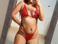 AntoniaBrunni in a shiny red bikini, showing her boobs and pussy with a high-cut bottom, taking a mirror selfie, hand on hip, red hair, tan skin.