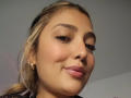 BiancaRey with light brown skin, blonde hair in a ponytail, wearing gold earrings, and glossy pink lips, smiling slightly, showing subtle makeup, and a confident expression.