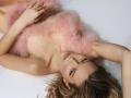EolantaMarina lying on a white surface, wearing a pink furry wrap that covers her tits, with blonde hair spread out, looking up with a relaxed, sexy expression.