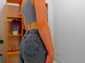 Steisii has a cute ass in grey denim jeans and a grey sports bra, standing with her back to the camera in a room with wooden shelves.