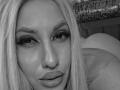 VickiSpices has blonde hair, a nose piercing, and full lips with a slight smile. Her eyes are lined with dark eyeliner. Her ass is partially visible in the background.