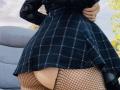 KarKutie's black checkered dress, flaring out to reveal fishnet stockings and her bare, round ass. She's standing outside, hand on hip, wearing a black lace top.