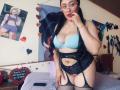 CristalZafiro with long black hair, glasses, light blue bra, black lace garter, and fishnet stockings, standing in bedroom, biting her finger, showing her tits and ass.