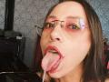 NoemiPrettiest with glasses, red eyeshadow, and pink lipstick, tongue out, saliva dripping, looking up, in a selfie. She has dark hair and a slightly open mouth.