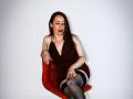 SweettEve with red velvet chair, brown dress, black thigh-highs, and red lipstick, sitting, looking down, right hand on chair, left hand on knee, white background, photo.