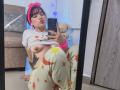 HairyValeri with pink headband, white shirt lifted to show tits, colorful star-patterned pants, sitting in front of mirror, taking selfie with phone, fluffy teddy bear in background.