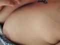 MirandaDreams' bare tits, showing a small tattoo near her left breast, with her hand slightly touching her skin. The image is a tight, upper-body shot.