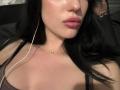 BessieSevcik's face with pouty pink lips, black hair, light skin, subtle shine, small necklace, white earbuds, wearing a purple top, showing her tits slightly.