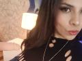 VioletaStone with long dark hair, wearing a black top with cutout holes, pink dildo in left hand, looking at camera, slightly pouting lips, thick black eyeliner, gold necklace.