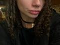 HotCaramelsTrio with curly brown hair, wearing a black choker with a cross pendant, has a nose ring and lip ring, and is pouting with pinkish lips.