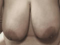 ZoeHotXX's large, hanging tits with dark nipples and a pierced nipple on top. Her light brown skin is visible, showing some stretch marks. The image is a photo.