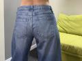 Stefanni's blue denim ass is in the frame, showing two back pockets and a slightly worn texture. A green couch is partially visible on the right.