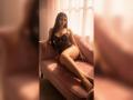 MiilaWx with long brown hair, lace black lingerie, and a pink velvet couch, legs crossed, arms resting, soft sunlight, sexy, bare feet, confident, warm, relaxed.