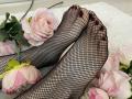 MiraRosse's feet in black fishnet stockings, with dark red toenails, resting on pink roses. Her toes are slightly curled. Soft white rug underneath.