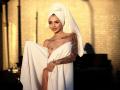 KayaBelle with a white towel wrapped around her body, covering her tits, but exposing her nipples. She has tattoos on her right arm and a towel on her head.