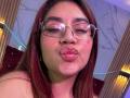 ValmontAlessia with puffy pink lips, wearing glasses, nose ring, and red hair, making a pouty face, showing her soft, round tits, and a slightly chubby face.
