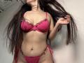 Tisia in pink lace lingerie with floral embroidery, holding her long brown hair, exposing her tits and pussy, standing with her ass slightly tilted.