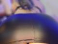 Kkole's shiny black leather ass is the focus, with a subtle seam running vertically down the center. Blurred upper body in the background.
