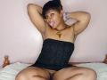 RareGem with dark skin, short black hair, and armpit hair, wearing a black strapless dress, tongue out, arms raised, sitting with legs spread, showing her pussy.