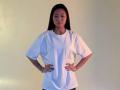 JeseniaMichalczik stands with hands on hips, wearing a loose white shirt, long black hair, and a tattoo on her right arm. She's looking straight at the camera.