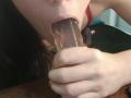 La bouche d'OrianaLaFrancaise est entourée d'un sextoy translucide, et sa main serre la base. Son soutien-gorge rouge est visible. Ses cheveux foncés sont partiellement cadrés..