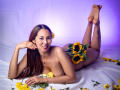 Rosalinda Cortez ist nackt und liegt auf dem Bauch, wobei Sonnenblumen ihre Brüste und ihre Vulva bedecken. Sie hat langes, braunes Haar, eine Blume im Haar und ein Tattoo an ihrem Oberschenkel..
