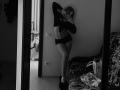 BobbyeWelson stands in front of a mirror, taking a selfie. She's wearing a long-sleeve top and black panties, showing her bare ass and small tits. Black-and-white photo.