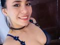 LucieMilner with dark hair, smiling, wearing a blue sheer bra with flower accents, black choker, and dangling earrings, showing her tits. She has a cute face and red lipstick.