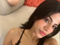 EvaGate has dark brown eyes, pink lipstick, and black hair, looking at the camera with a slight smile. She's wearing a black lace top, showing her tits.