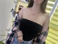 Nesie with bare shoulders, black strapless top, pink plaid shirt off, blue jeans, necklace, pouty lips, long brown hair, butterflies on white shelf, stuffed tiger, window blinds.