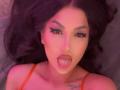 ItsJessieBabe mit dunklem Haar, rotem Eyeliner und einem Nasenring, die ihre pinke Zunge herausstreckt, ein rotes Oberteil trägt und eine kleine Tätowierung auf ihrer Brust zeigt..