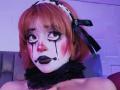 ViolettClay with orange hair, white face paint, black tears, red cheeks, black lipstick, and a black lace choker, looking shocked with black ribbon in hair.
