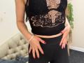 Stefanni with tan skin, wearing black lace top revealing her small tits, black pants, red nail polish, white bracelet, hands on her ass, in a bedroom.