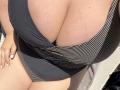 Barbarica's huge tits in a black and white striped one-piece, sunlit skin, white-painted nails resting on her thigh, hand partially visible.