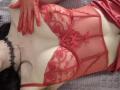 Rozalin in red lace lingerie with matching gloves, showing her tits, wearing a black choker, lying on a gray textured surface. Her hands are resting on her chest.