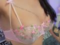 FrenchShanna's pink floral bra with visible nipples, sheer mesh, and pink ribbons, showcasing her tits and tattoo on her right shoulder. Black hair, tattooed arm, and purple light.