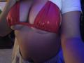 AntoniaBrunni's big, shiny red bikini top barely covers her huge, round tits, with a white shirt pulled up. Her belly is exposed, and she's holding the top.