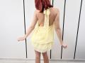 JuliannaMoor with red hair, back to camera, wearing a yellow halter dress that exposes her ass, standing in a white room with black lines.